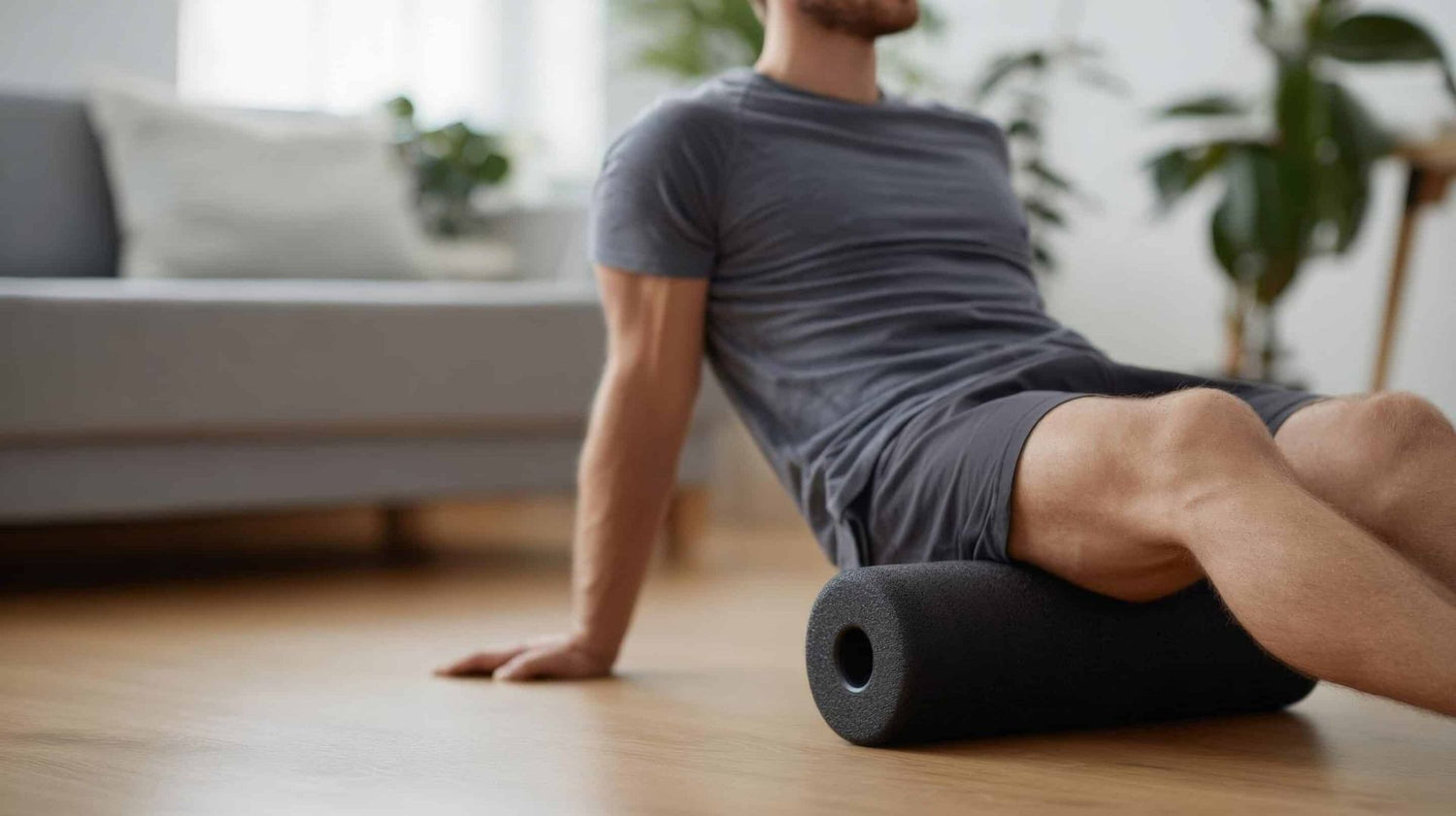 Man using a foam roller on a wooden floor in a living room.