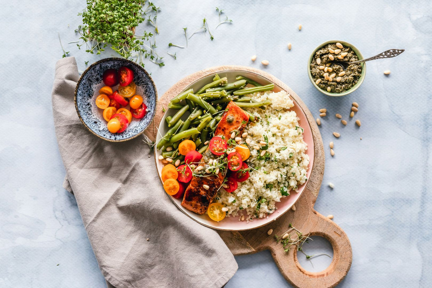 Colorful salad with quinoa, green beans, cherry tomatoes, and nuts on a light gray background.