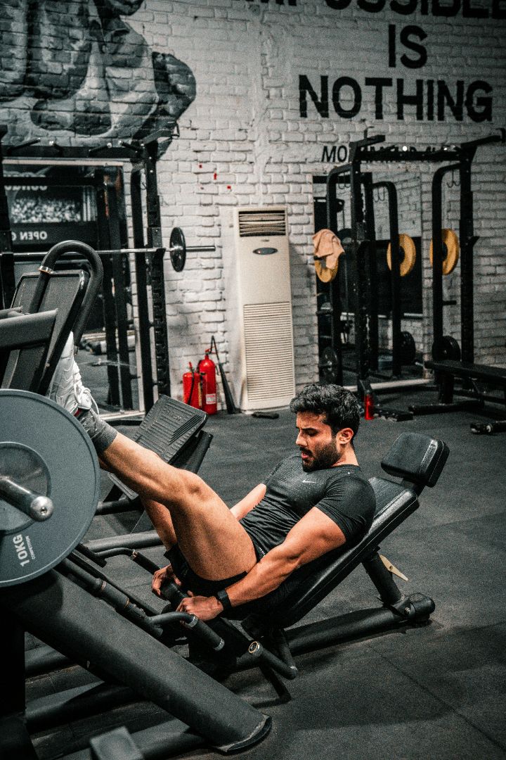 Man exercising on a leg press machine in a gym with motivational wall art.