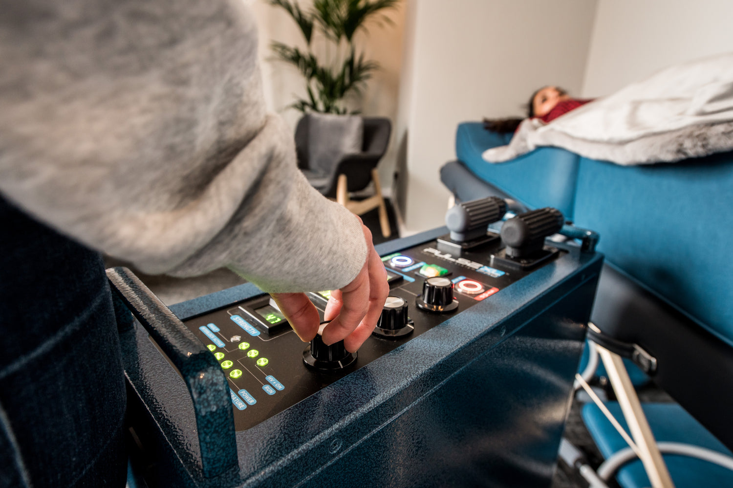Person operating a PEMF control panel with a patient lying on a bed in the background